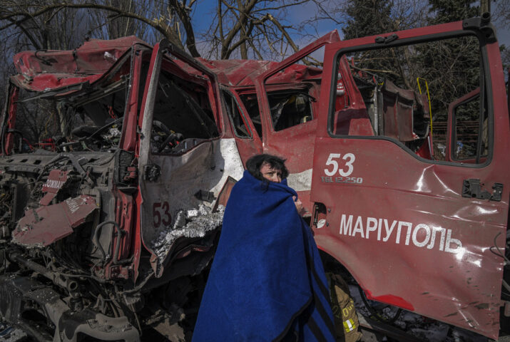 A women covers herself with a blanket near a damaged fire truck after shelling in Mariupol, Ukraine, Thursday, March 10, 2022. (AP Photo/Evgeniy Maloletka)