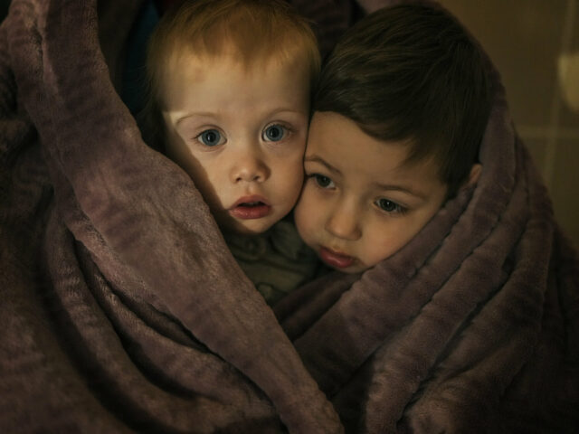 The children of medical workers warm themselves in a blanket as they wait for their relatives in a hospital in Mariupol, Ukraine, Friday, March 4, 2022. (AP Photo/Evgeniy Maloletka)