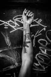 A young man stands for a picture showing his arm tattooed with a machine gun. Growing waves of violence are seen in many simple manifestations of daily life with a youth more and more related to violent beheavior as victims and victimizers.