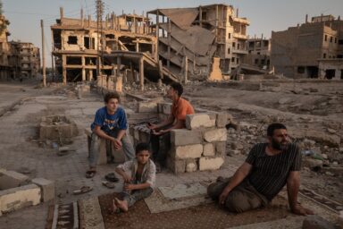 Abdelatif Daham Al Hummada (right) sits with his sons and nephew on the street outside their heavily damaged home, where the family often sleeps, in Deir al-Zour, Syria, August 20, 2025. Photo by Nicole Tung (VII Photo, for The New York Times)