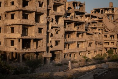 A woman walks through a damaged neighborhood in Deiral-Zour, Syria. Seventeen of the city’s 25 neighborhoodswere almost completely destroyed, August 21, 2025. Photo by Nicole Tung (VII Photo, for The New York Times)